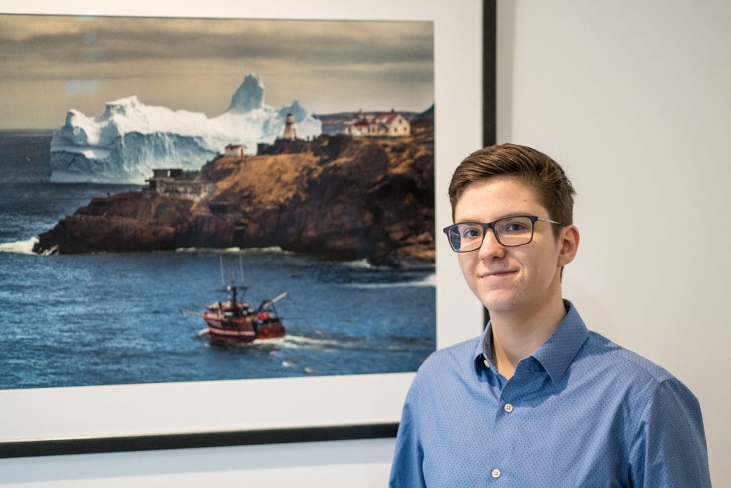 Naval Architect stands in front of photograph of a boat and glacier.