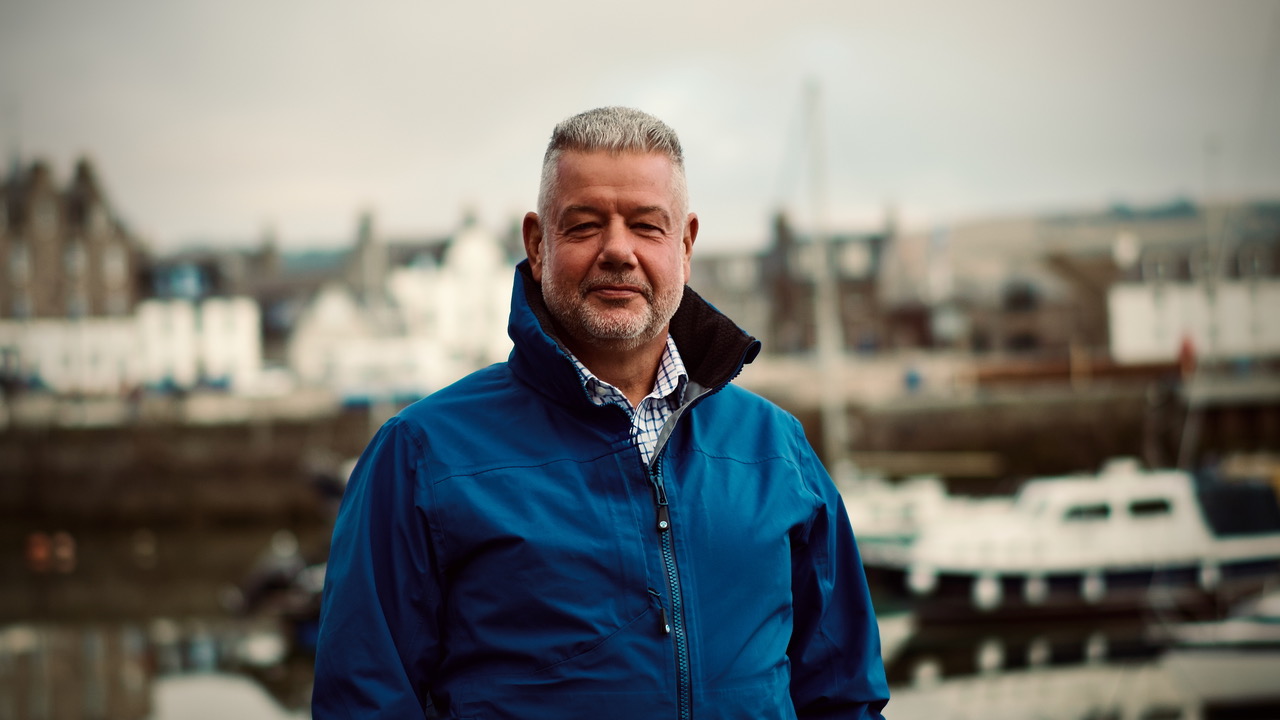 Man standing by harbour looking happily into camera