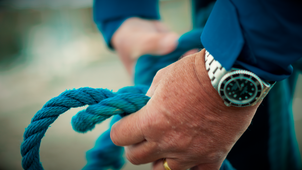 Macro view of sailor tying rope in knots, featuring a blue jacket and watch
