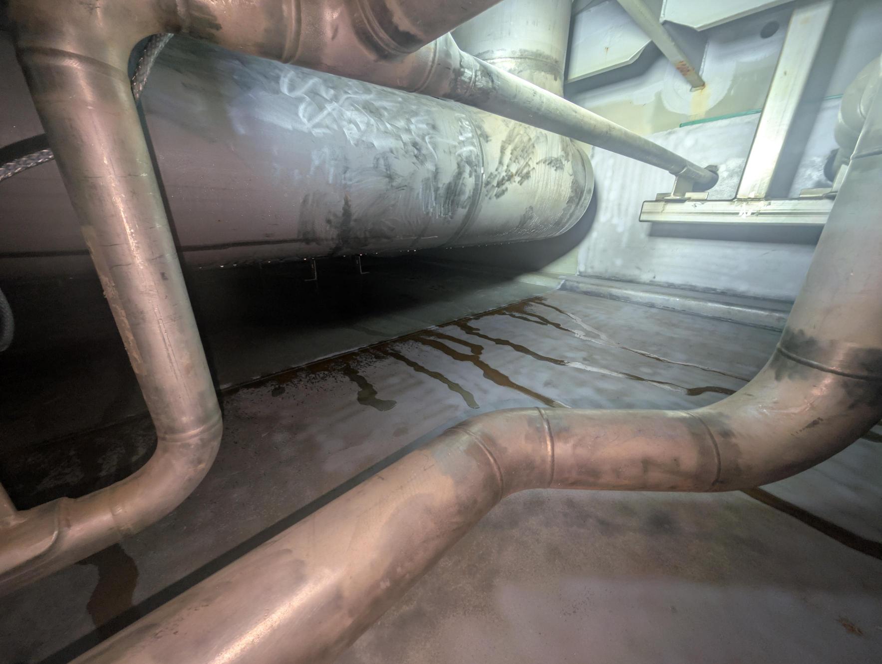 Condensation forming on in-service pipework inside a freshwater tank, with moisture draining onto tank surfaces and creating challenging atmospheric conditions during coating refurbishment works.